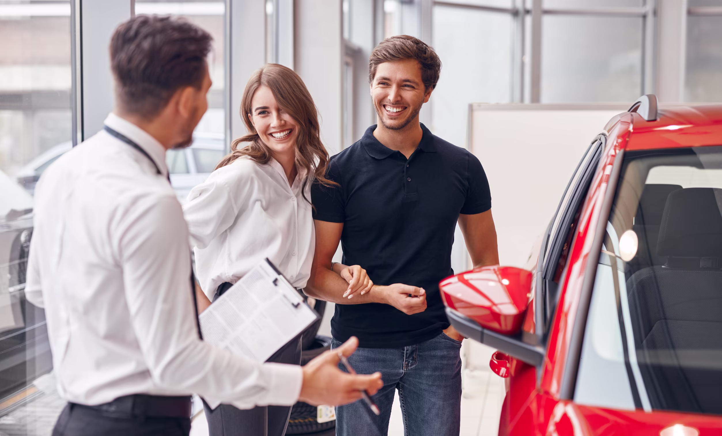 Couple discussing auto insurance options with a dealer near a red car