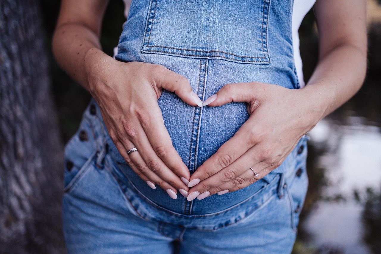 Pregnant woman in denim overalls forming a heart over her belly, illustrating life insurance protection for family.