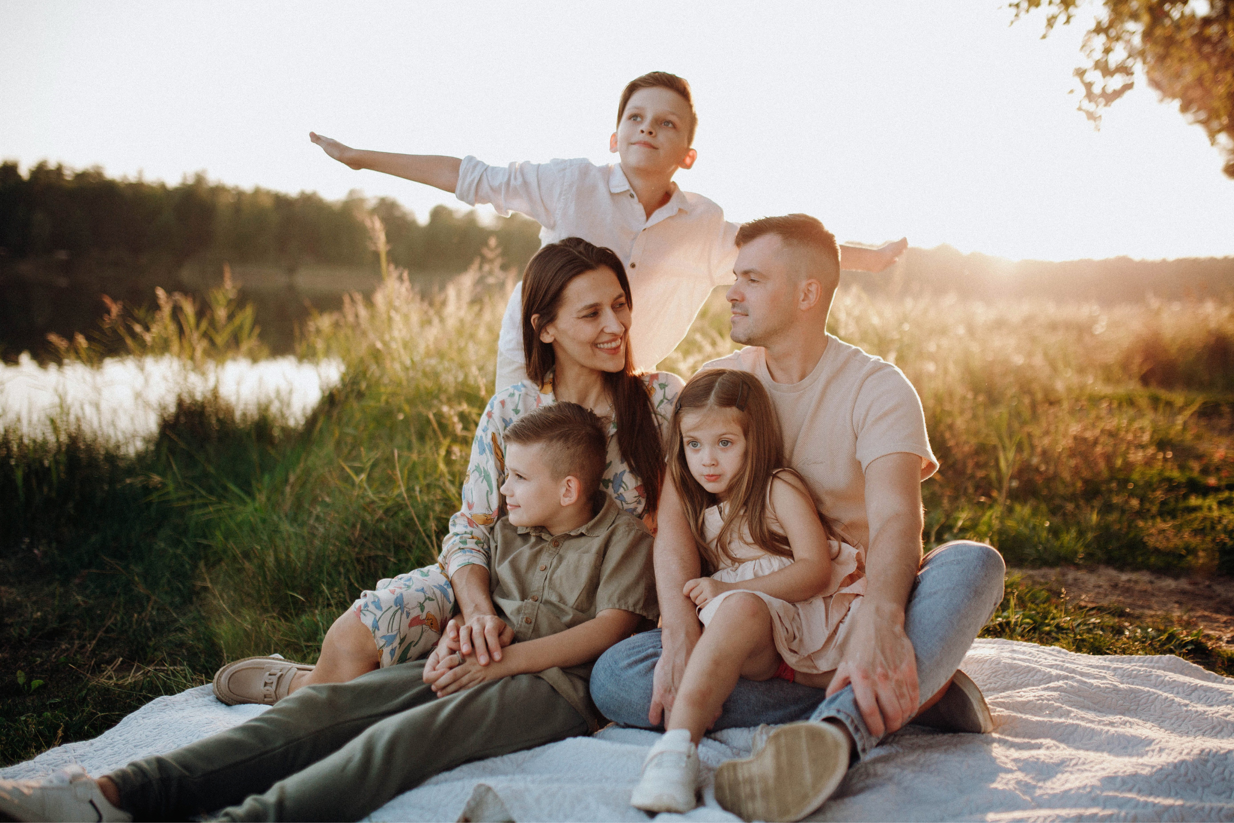 Family of five relaxing together outdoors at sunset by a lake